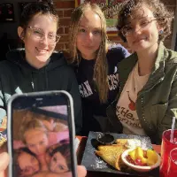 Sitting across the table from the three girls who are on the phone sucking his dick.